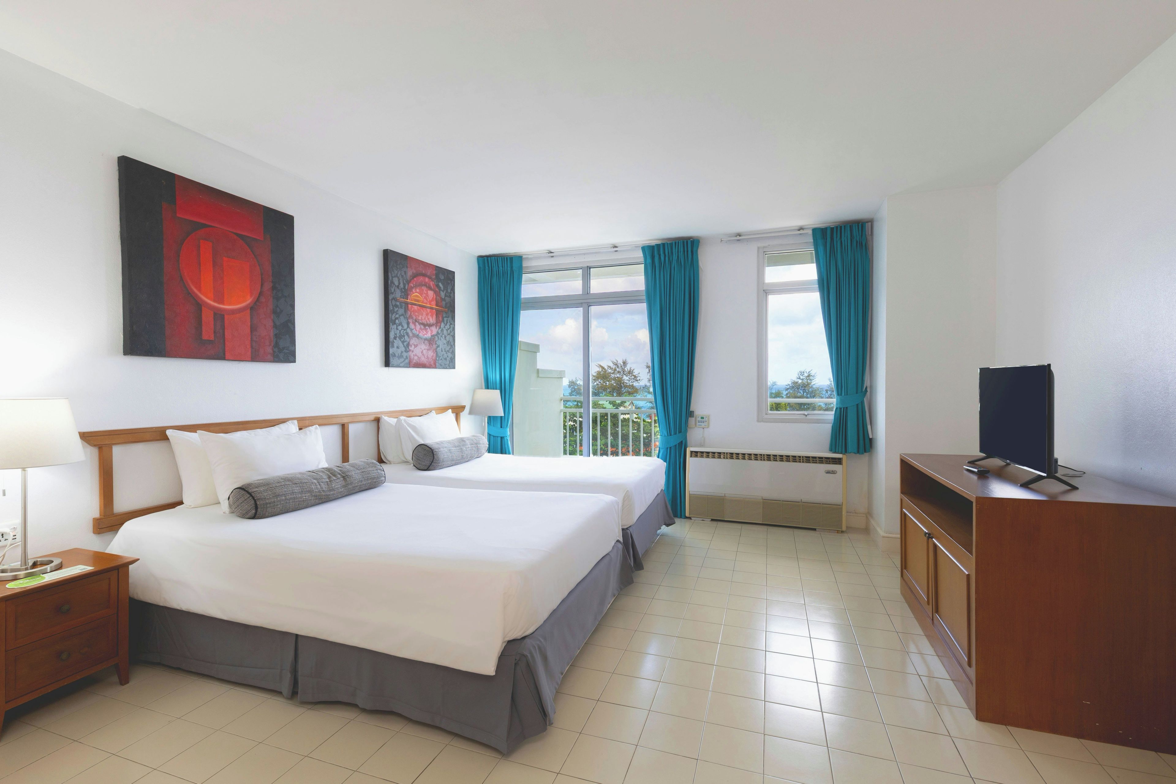 A hotel room with a bed, a TV, a desk, and a window with curtains.