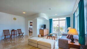 A modern living room with a sofa, chairs, a TV, and a balcony with curtains. - Waterfront Suites Phuket by Centara (Karon)