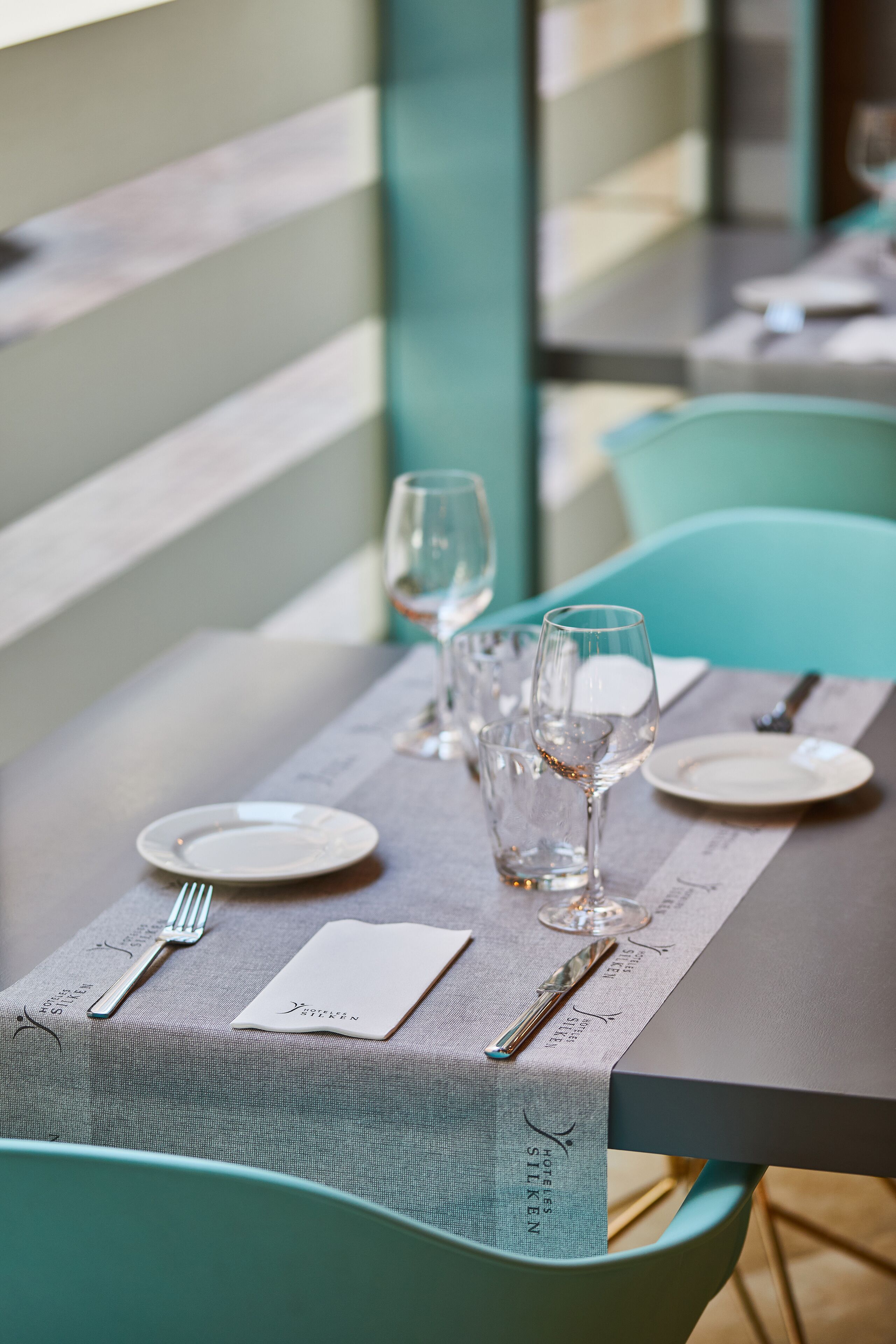 A neatly set dining table with a menu, glasses, and cutlery.