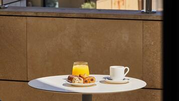 A balcony with a table set for breakfast, a glass of orange juice, and a cup. In the background, there are buildings with domed and spire structures.