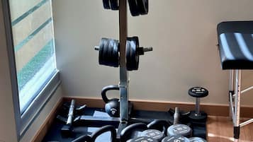 Un gimnasio en casa con un soporte para barra, kettebells, mancuernas y discos de pesas.