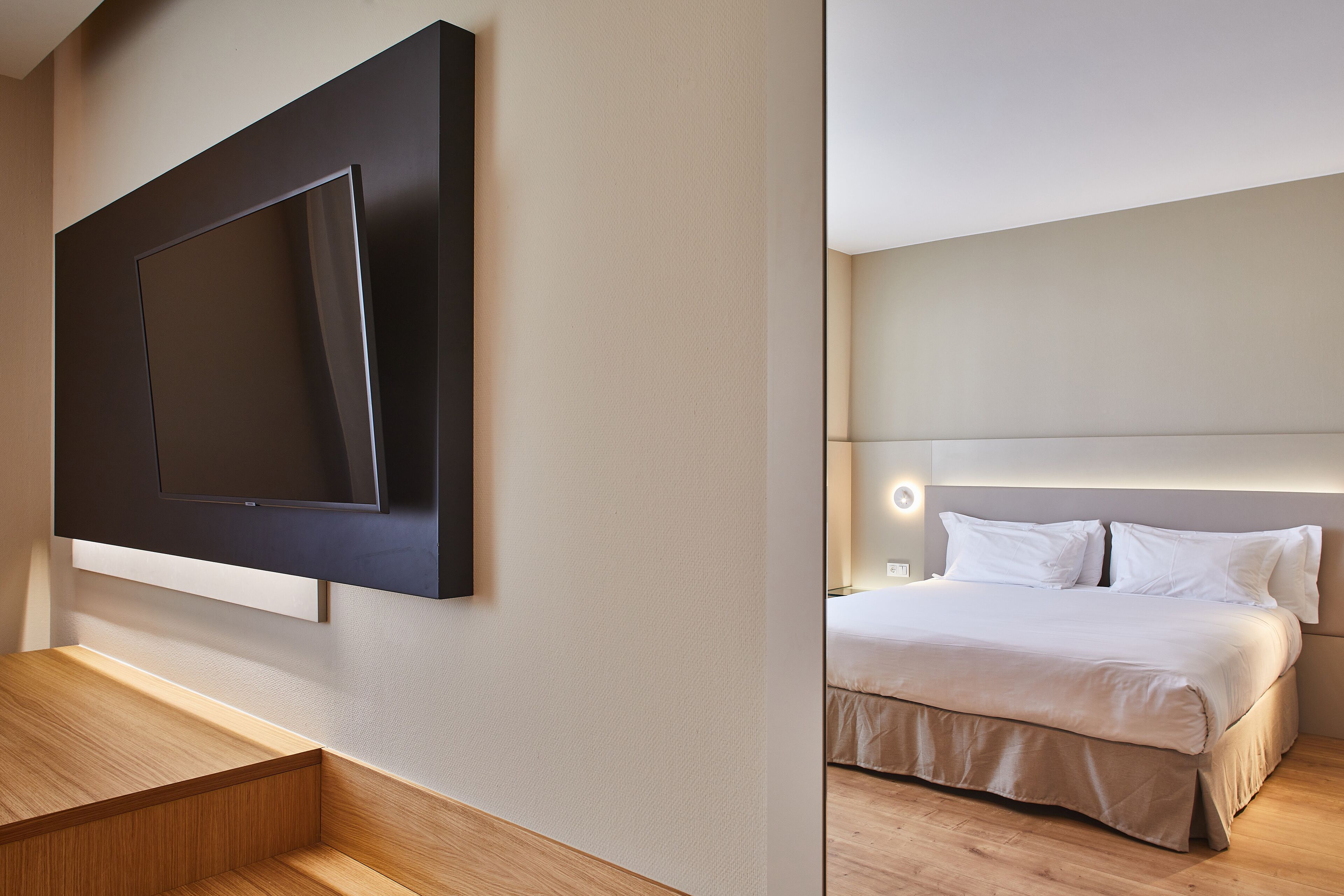 Una camera d'albergo moderna con una TV a schermo piatto montata a parete, una panca in legno e un letto rifatto con testiera.