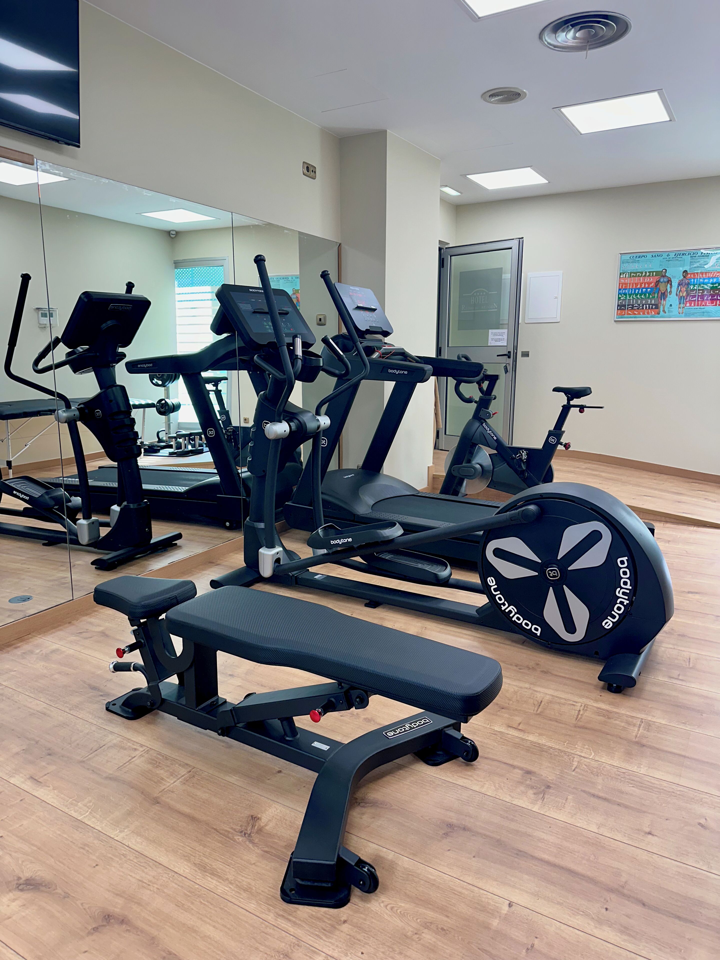 A gym with cardio machines, weight benches, and a mirrored wall.