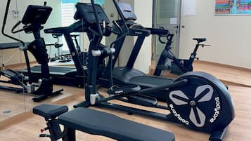 A gym with cardio machines, weight benches, and a mirrored wall.