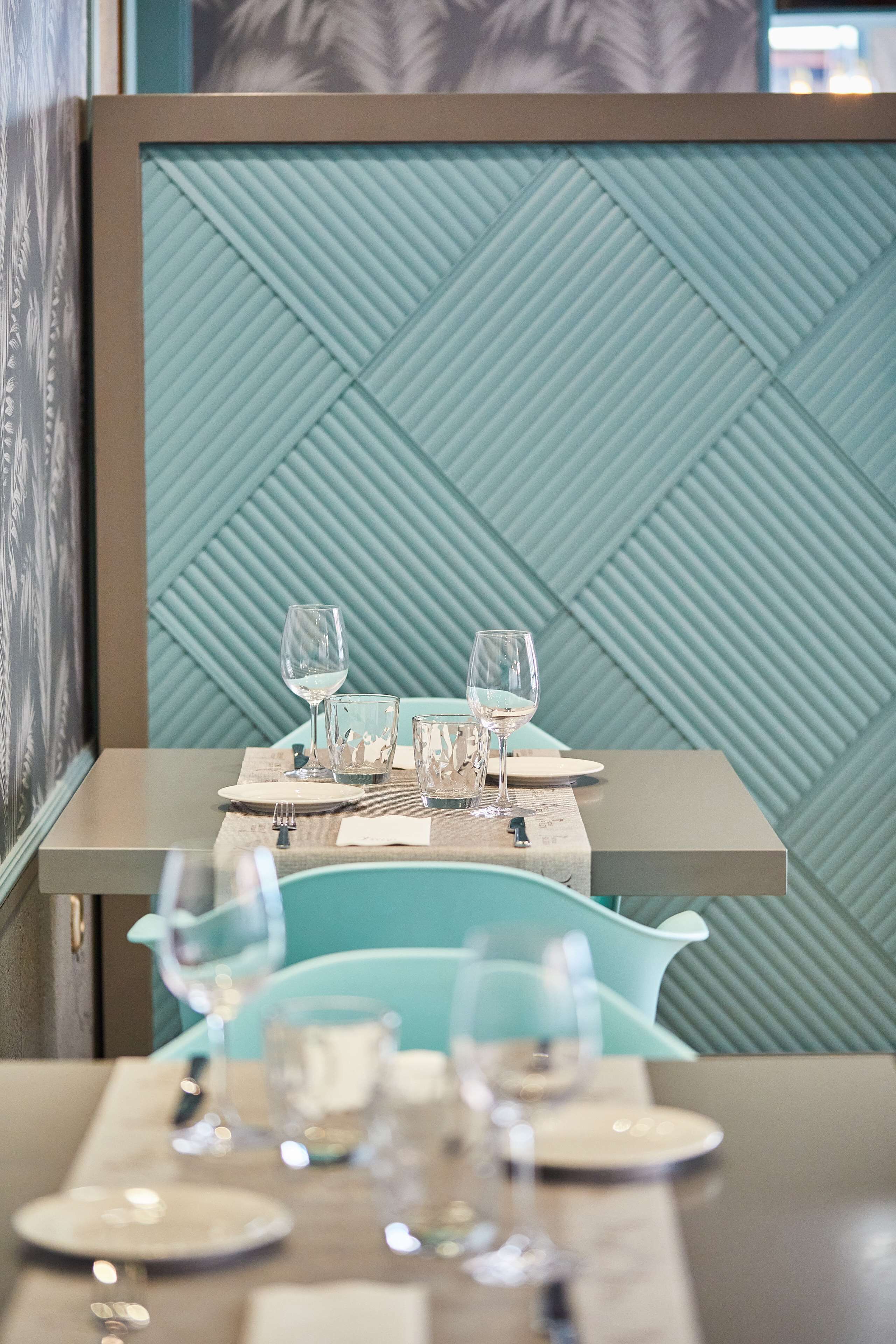 A dining area with a table set for two, featuring a teal-colored wall with a geometric pattern and a framed picture on the left.