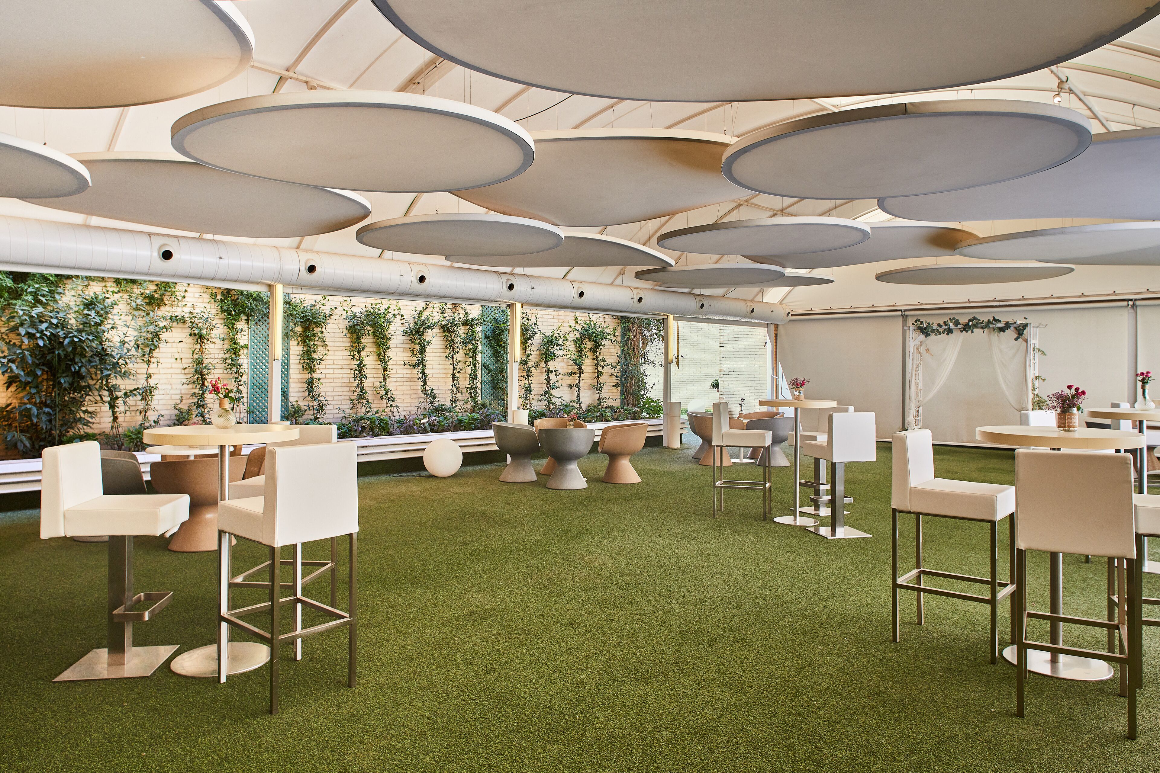 Un espacio interior moderno con mesas y sillas redondas, suelo de césped artificial verde e iluminación circular en el techo.