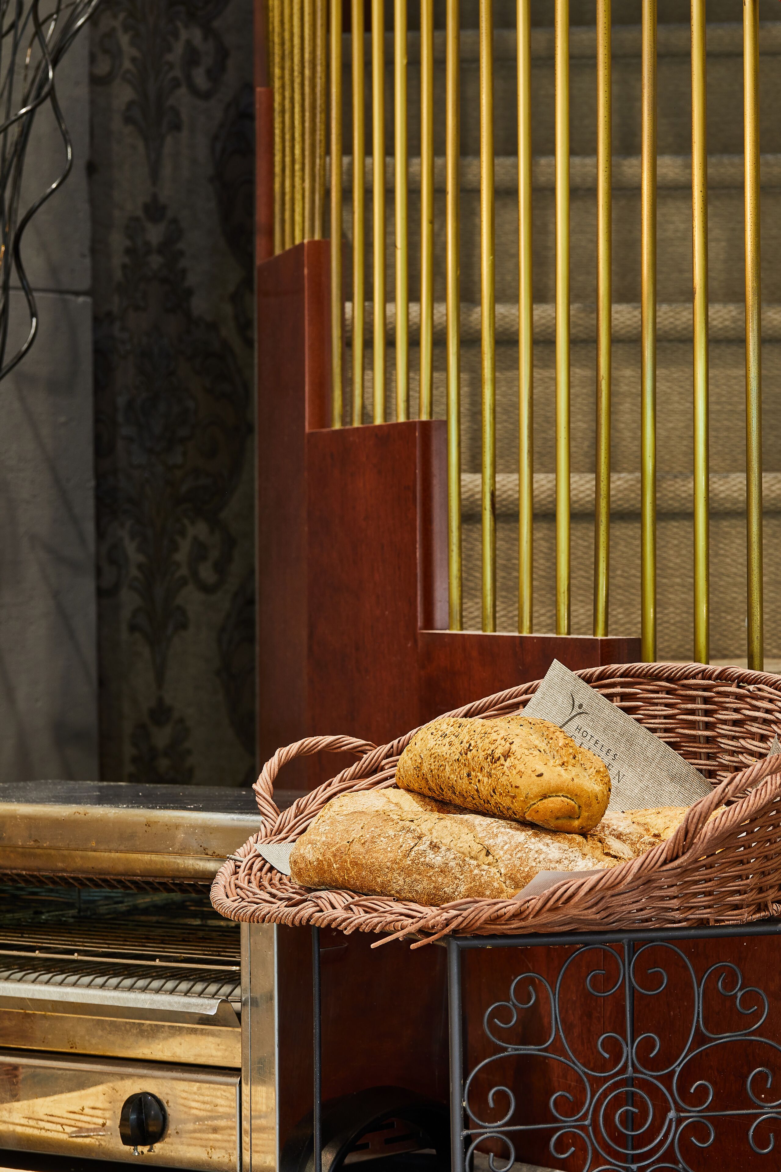 A wicker basket with bread on a wooden counter, a piano, and a patterned wall in the background.