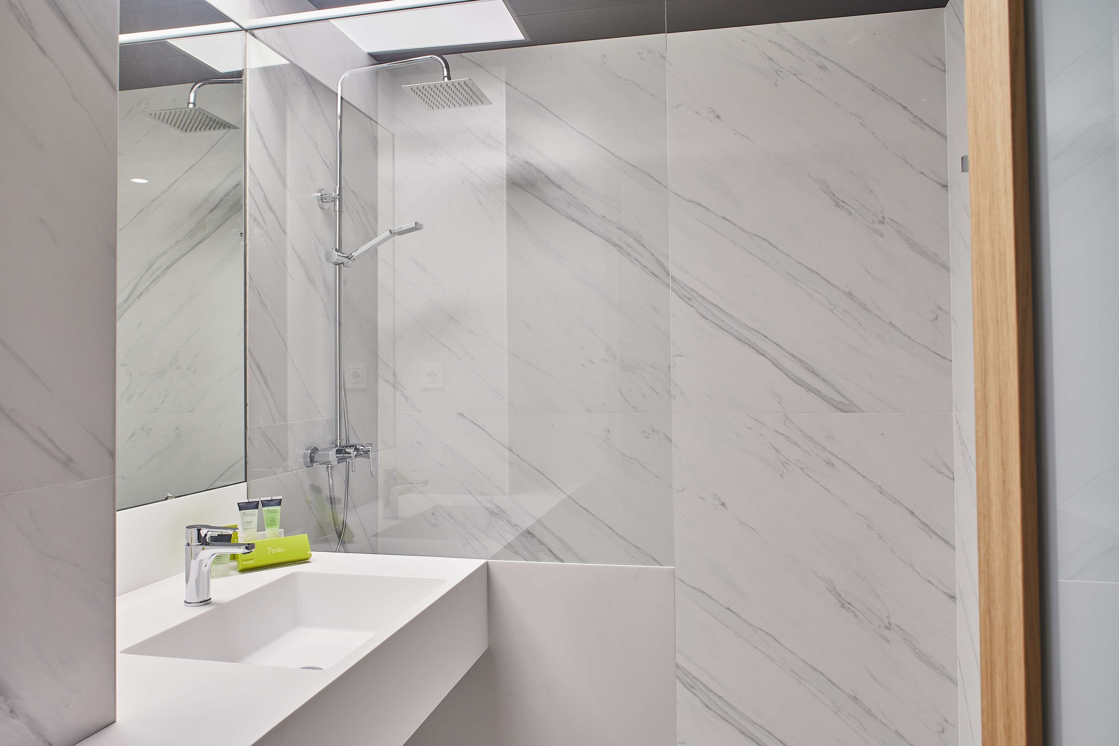 Un baño moderno con lavamanos blanco, cabina de ducha de vidrio y paredes de mármol.