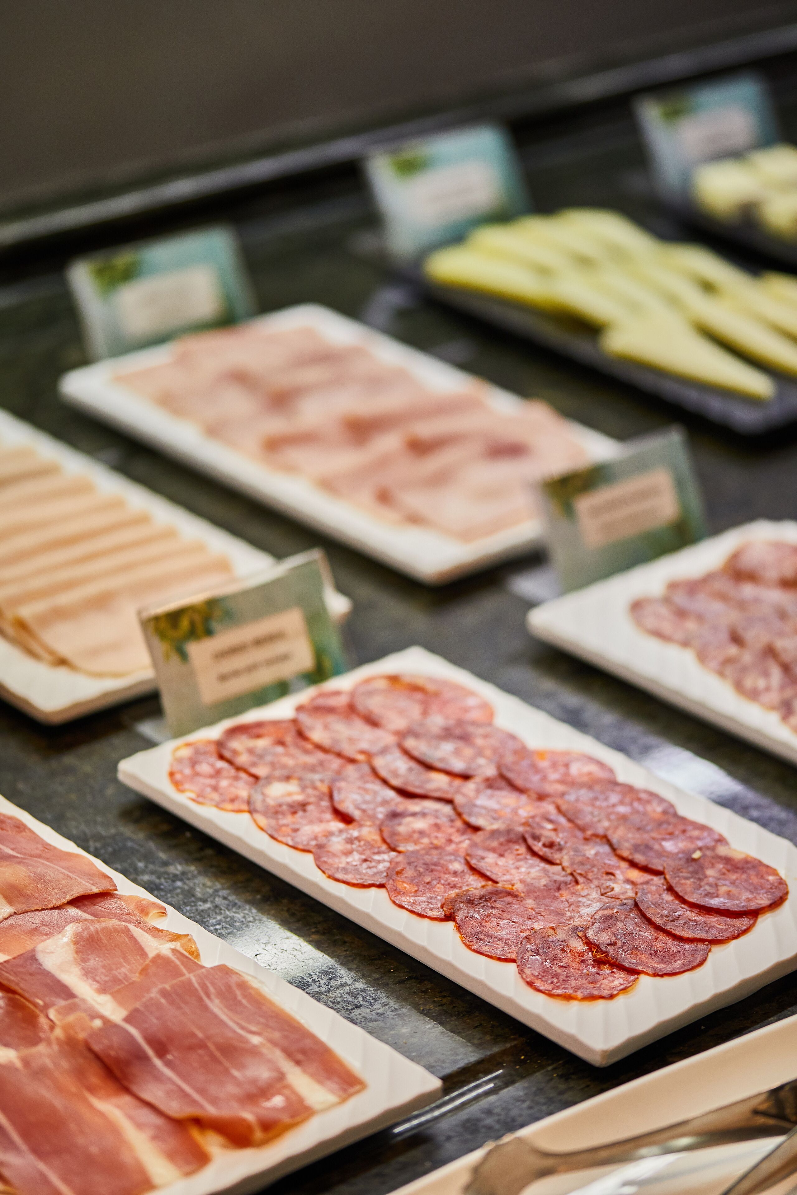 Una variedad de carnes cortadas en rodajas exhibidas sobre una barra.