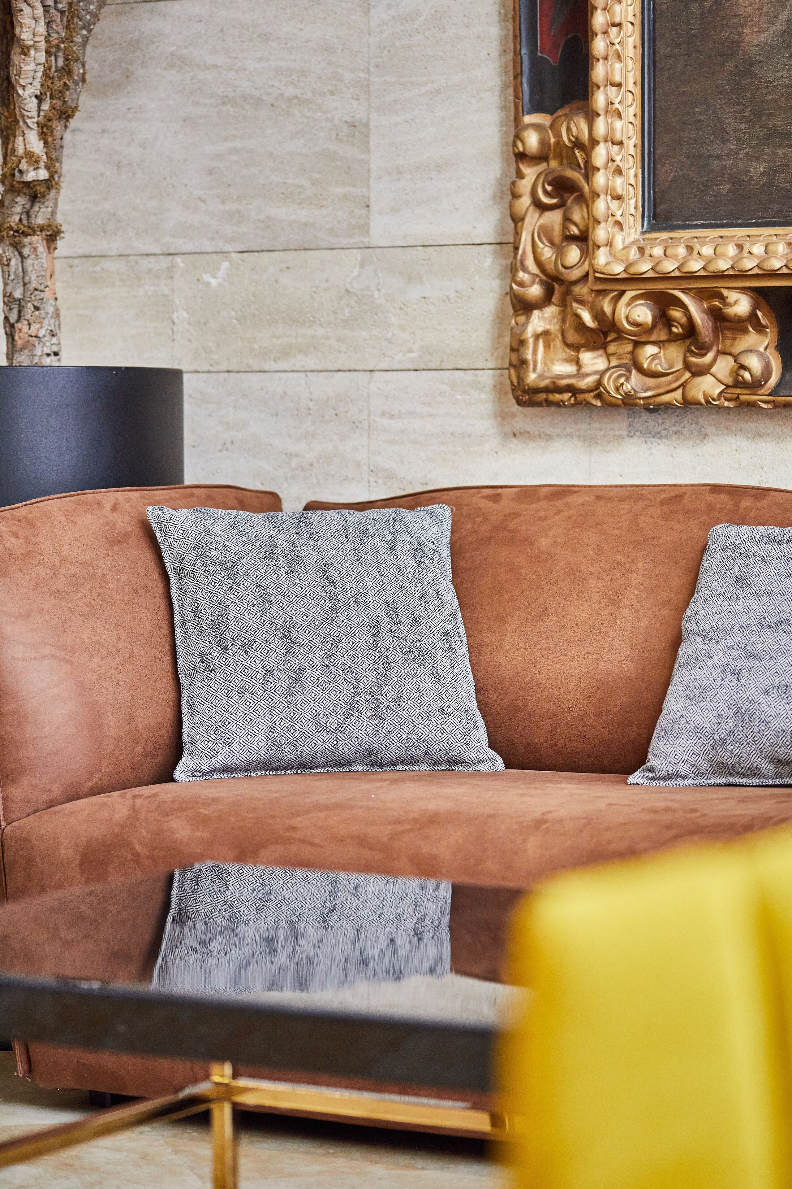 A brown leather sofa with patterned cushions, a gold-framed mirror, and a black floor lamp.