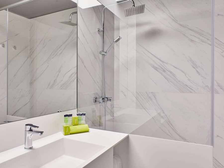 Un baño moderno con ducha separada por vidrio, lavamanos blanco y un espejo grande.