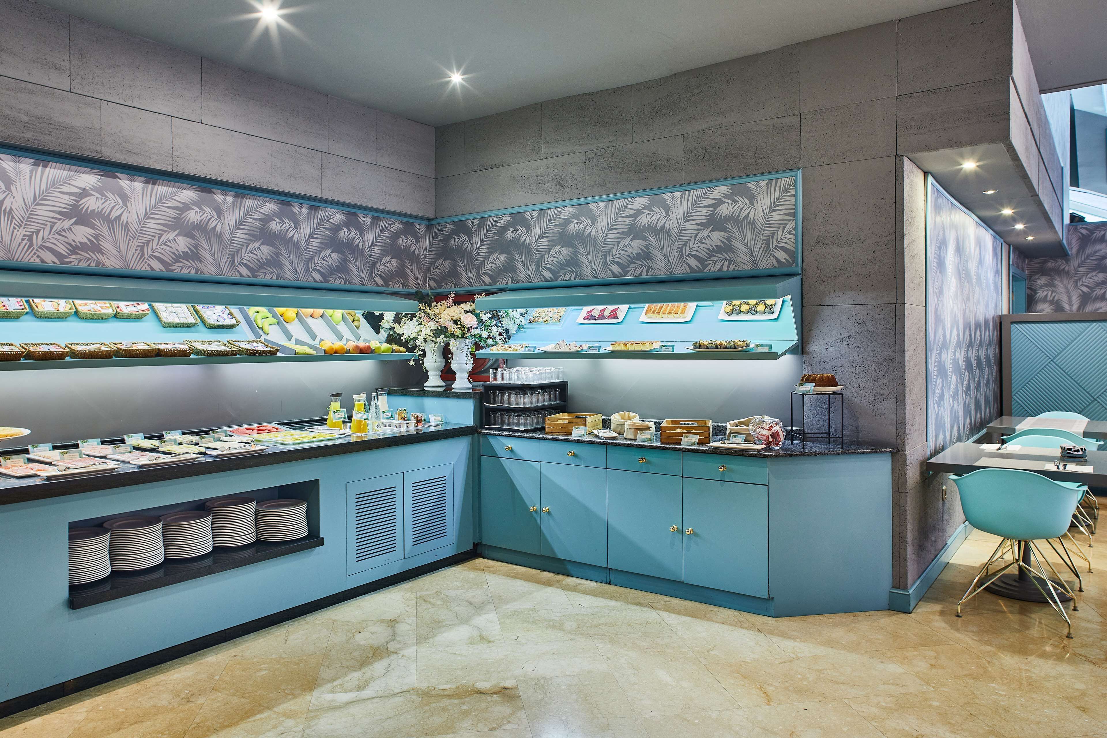 Una cocina moderna con armarios azules, encimera de mármol y diversos alimentos exhibidos en estantes.