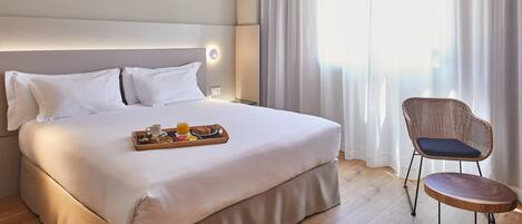 Un lit bien fait, avec un plateau de petit-déjeuner, une chaise en osier et une grande fenêtre ornée de rideaux légers.