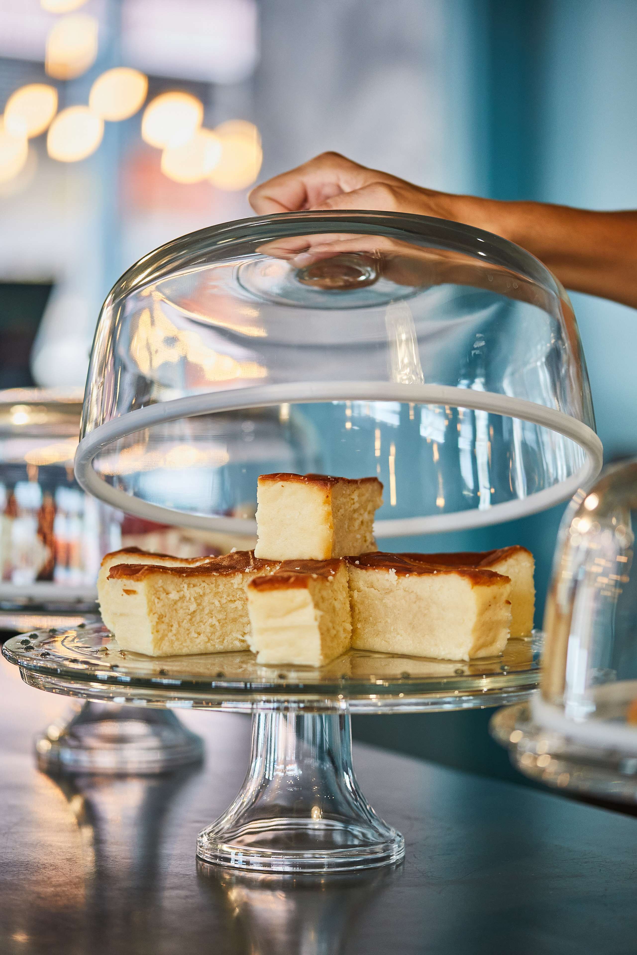 A glass cake stand with a transparent dome, holding several square pieces of cake.