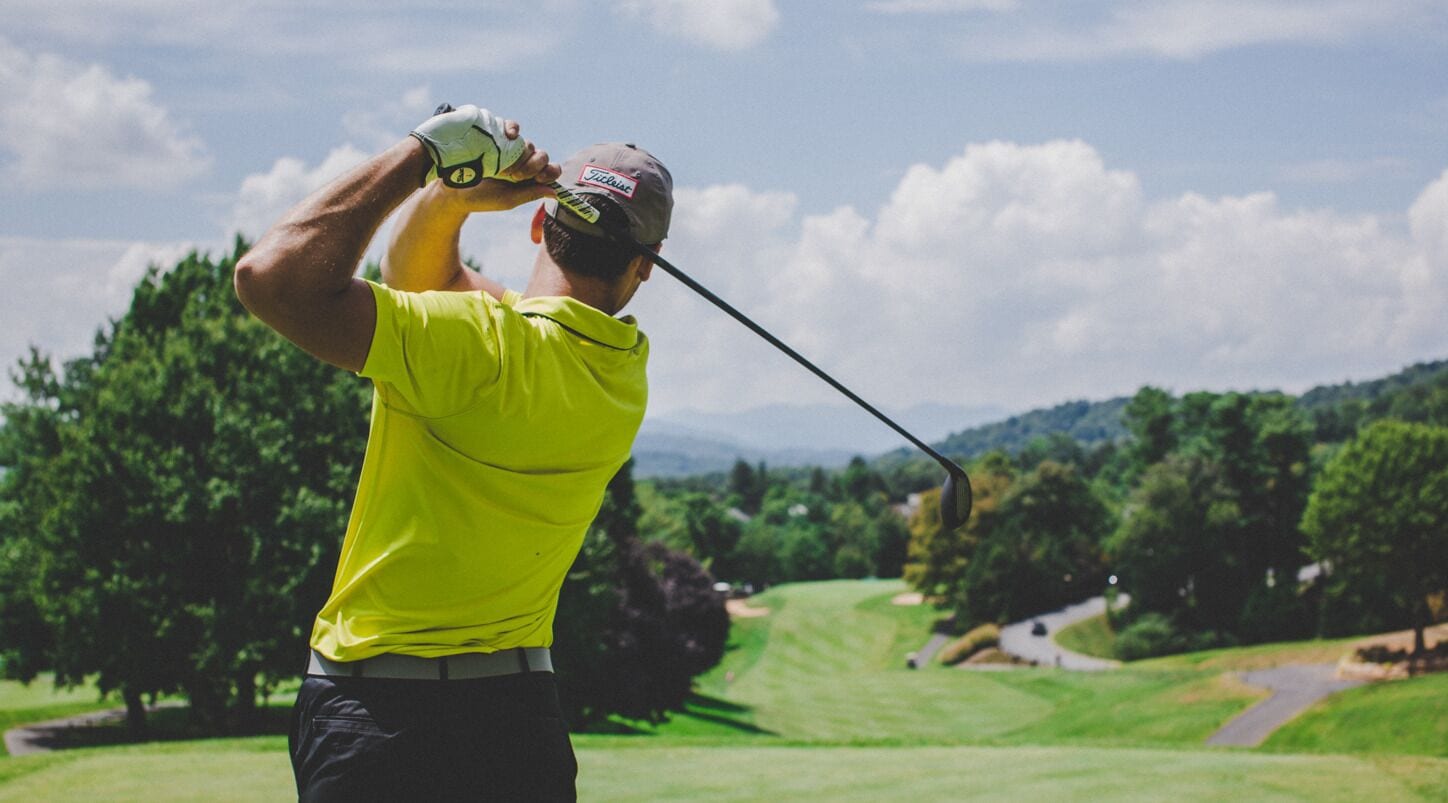 Une personne portant un t-shirt jaune vif et un pantalon noir, se préparant à frapper une balle de golf sur un terrain de golf.