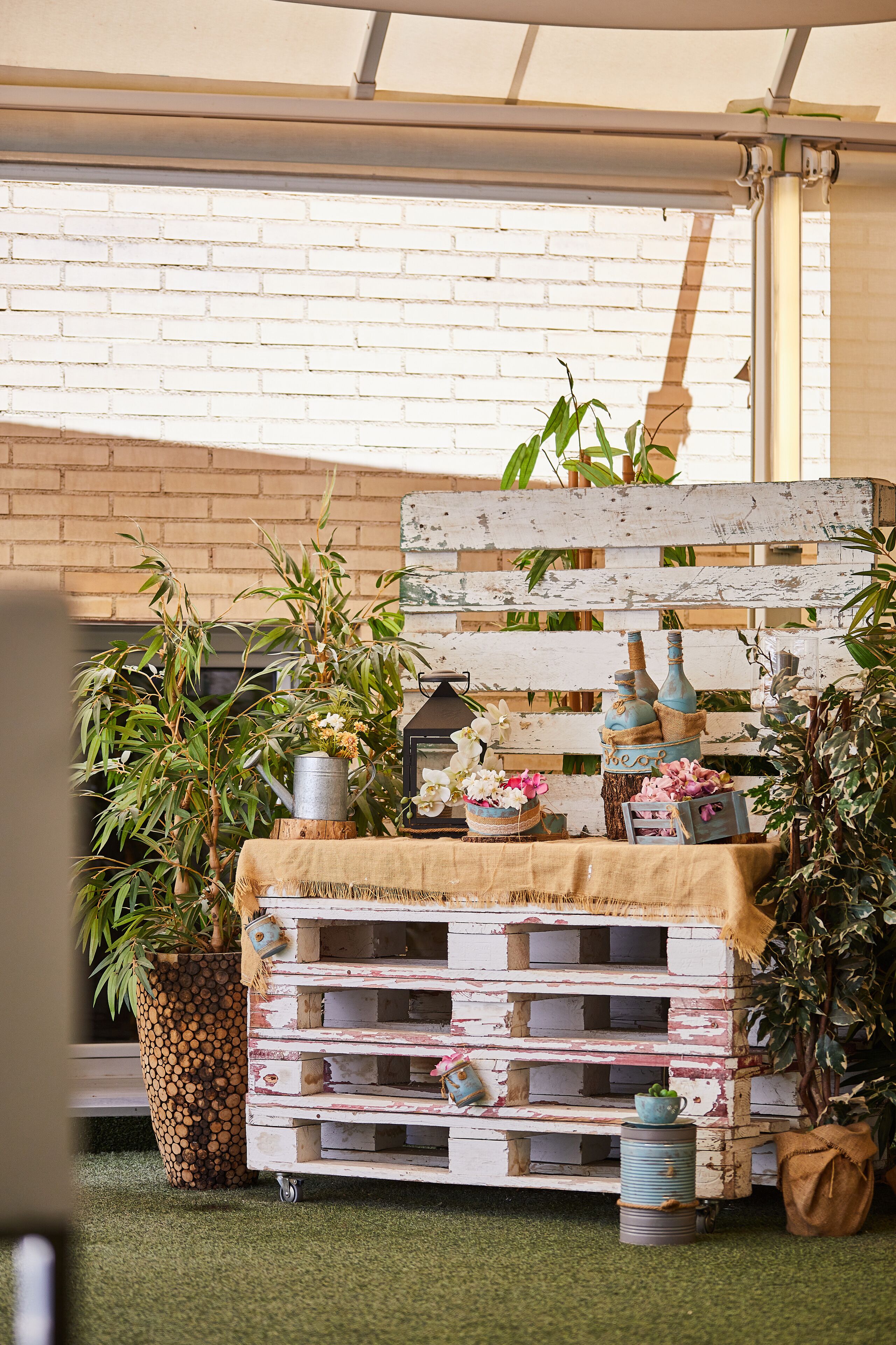 A rustic outdoor setting with a wooden pallet table, potted plants, and decorative items.