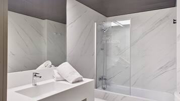 A modern bathroom with a marble wall, a white sink, a glass shower enclosure, and a toilet.