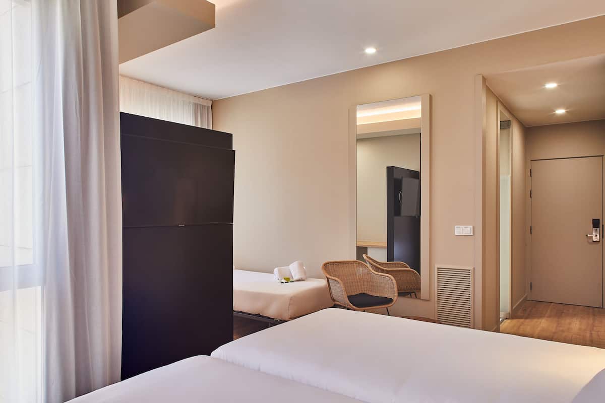 A hotel room with two beds, a large mirror, a wardrobe, and a chair.