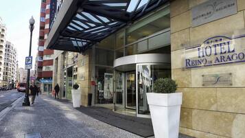 Entrada de un hotel con fachada de vidrio, un cartel que dice "HOTEL REINO DE ARAGON" y una señal de estacionamiento cerca.