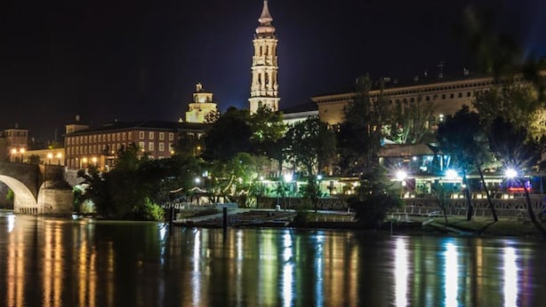 A nighttime view of a cityscape with a prominent tower, a bridge, and illuminated buildings. - Hotel Silken Reino de Aragón (Zaragoza)