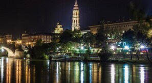 A nighttime view of a cityscape with a prominent tower, a bridge, and illuminated buildings.