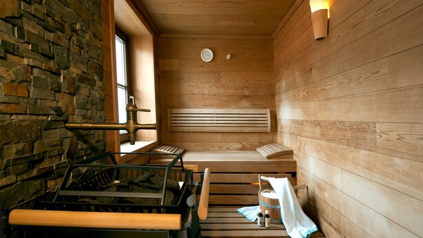 A sauna with wooden benches, a stone wall, and a window. - Hotel Bierwirt (Innsbruck)