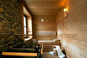 A sauna with wooden benches, a stone wall, and a window. - Hotel Bierwirt (Innsbruck)