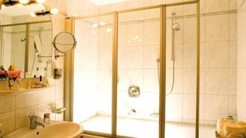 A modern bathroom with a glass-enclosed shower, a sink, and a vanity with a mirror and lights.