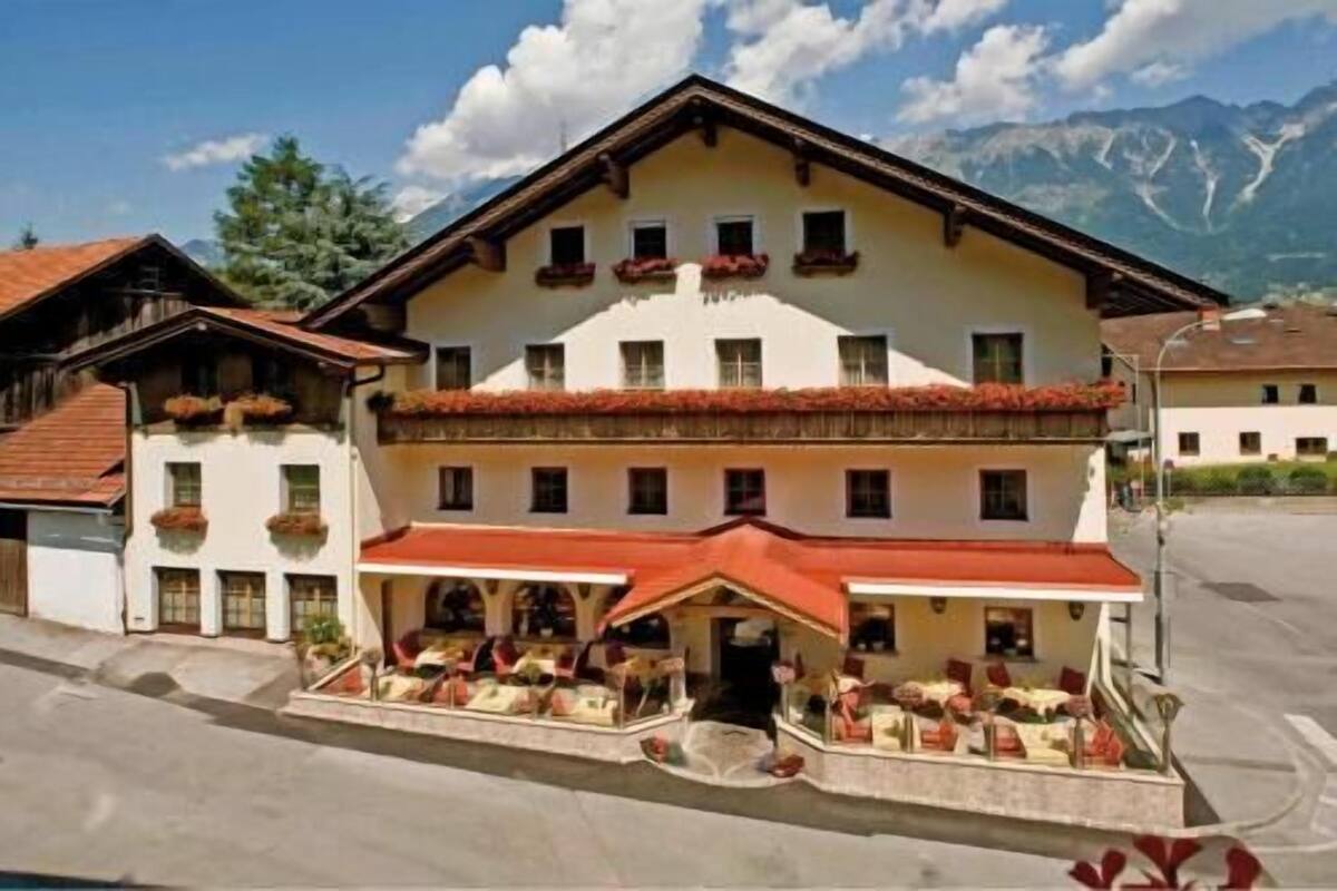 Un hôtel dont l’entrée est surmontée d’un toit rouge, qui possède de nombreuses fenêtres et qui est situé au pied d’une montagne.