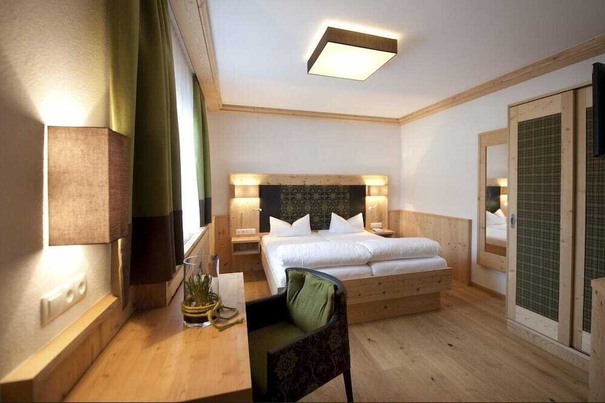 Une chambre d’hôtel comprenant un lit, des tables de chevet, un bureau, une chaise, un miroir et une fenêtre avec des rideaux.