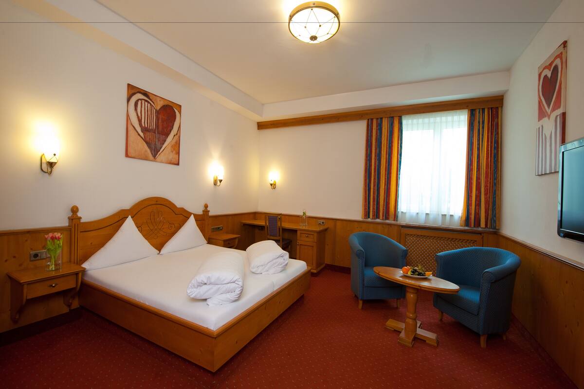 Une chambre d’hôtel avec un lit en bois, un bureau, une chaise, une télévision et une fenêtre avec des rideaux.