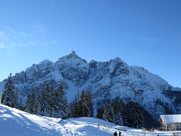 A snow-covered mountain with a ski resort in the foreground, including a building with a red roof and a sign that reads "Eingang".