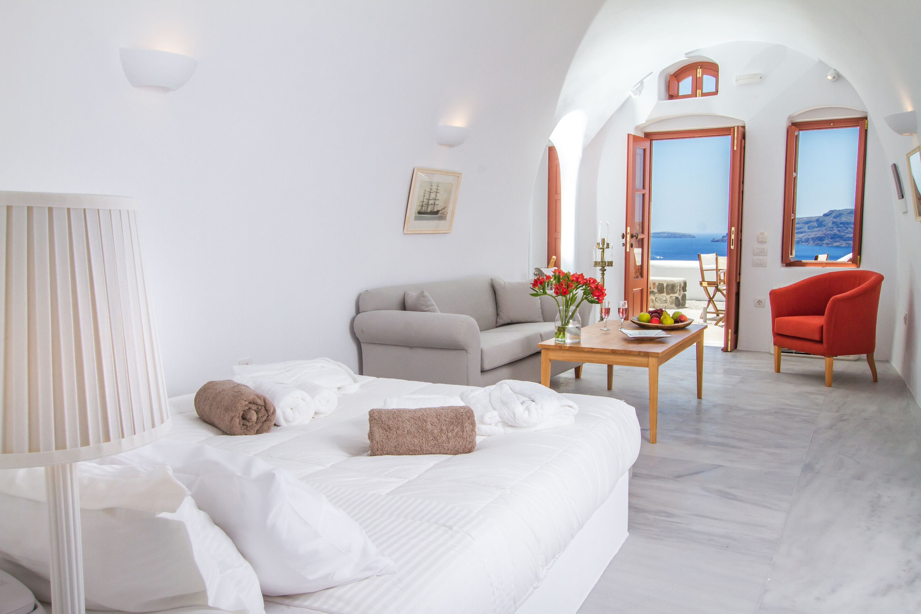 Habitación de hotel con cama, sofá, mesa con fruta y vista al mar.