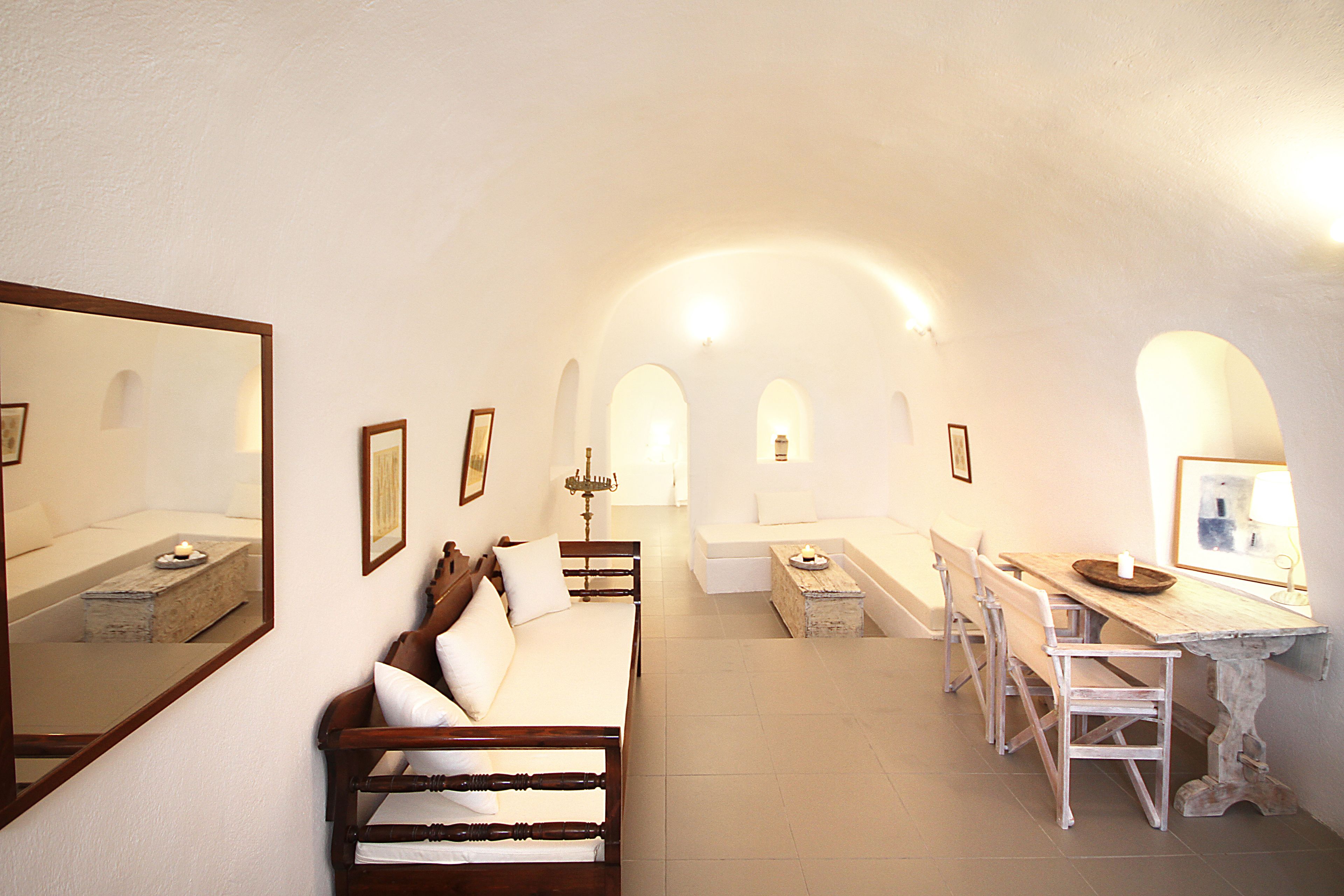 A room with a bed, a wooden bench, a dining table with chairs, and a mirror on the wall.
