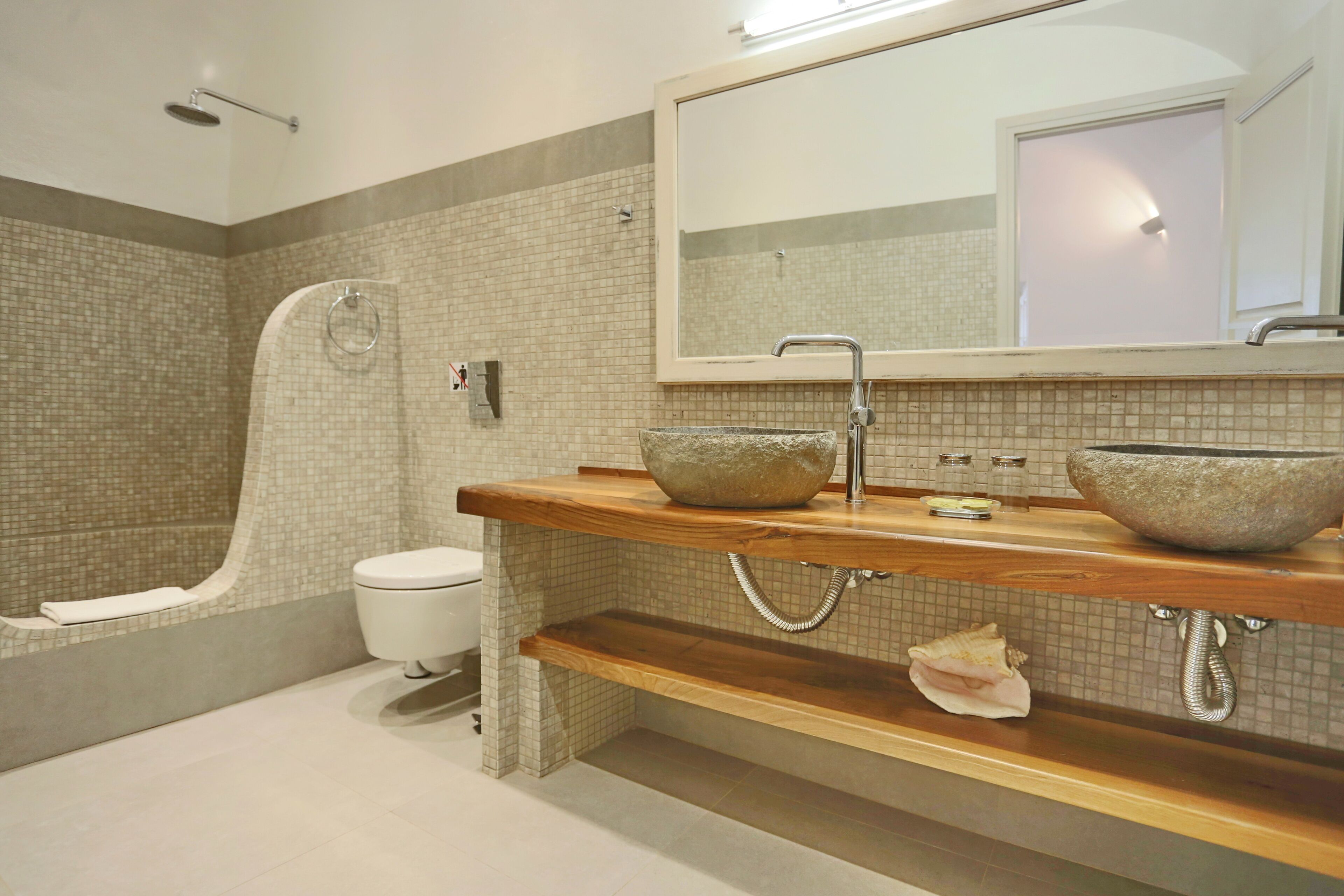 Un baño moderno con ducha, inodoro y dos lavamanos de piedra sobre encimeras de madera.