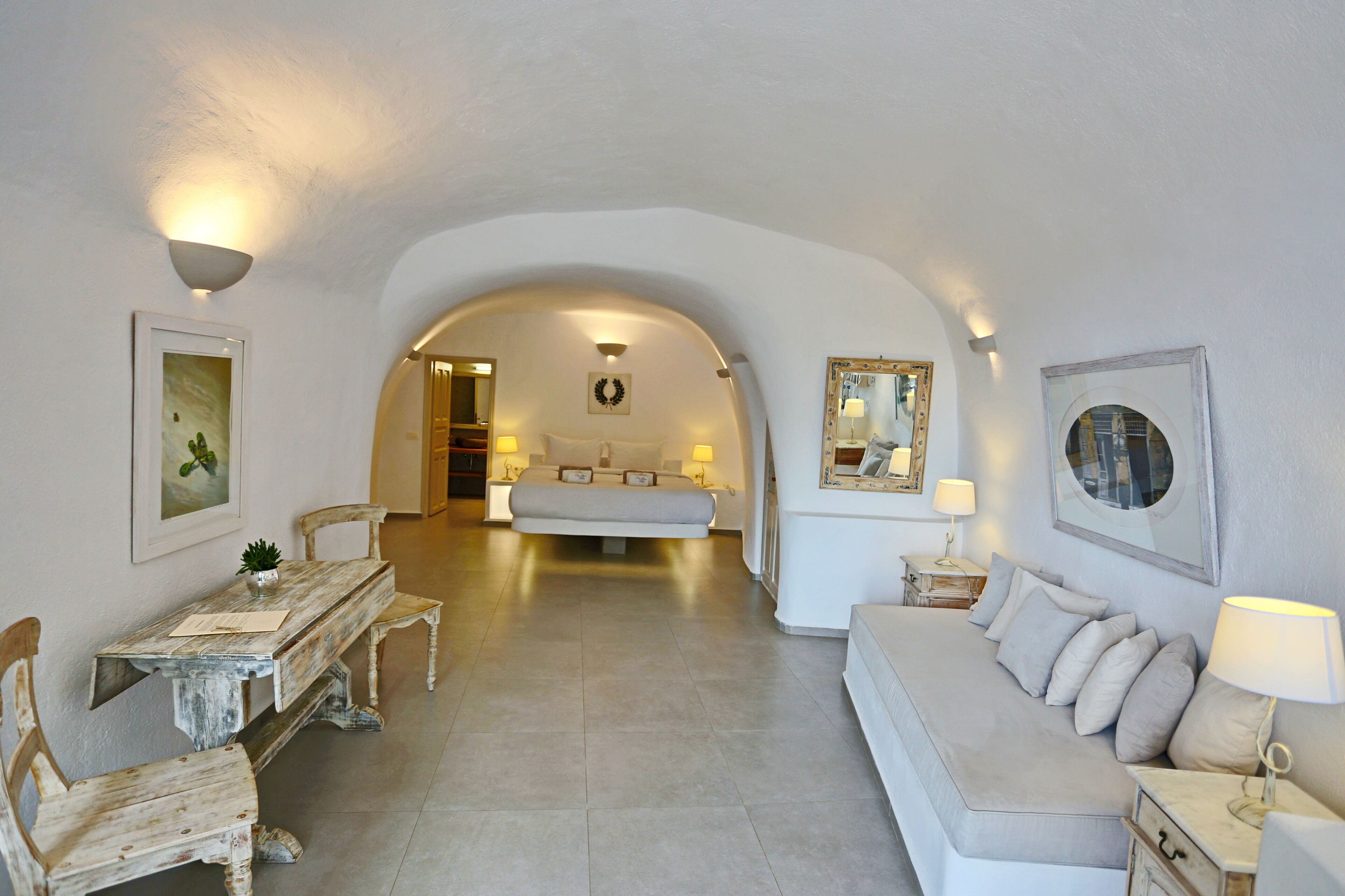 A room with a bed, a sofa, a dining table with chairs, and a small table with a lamp.