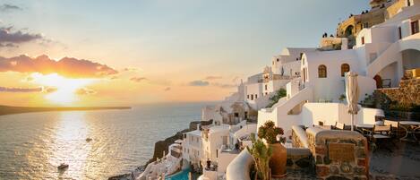 A coastal town with white buildings, a stone pathway, and a clear view of the sea at sunset.