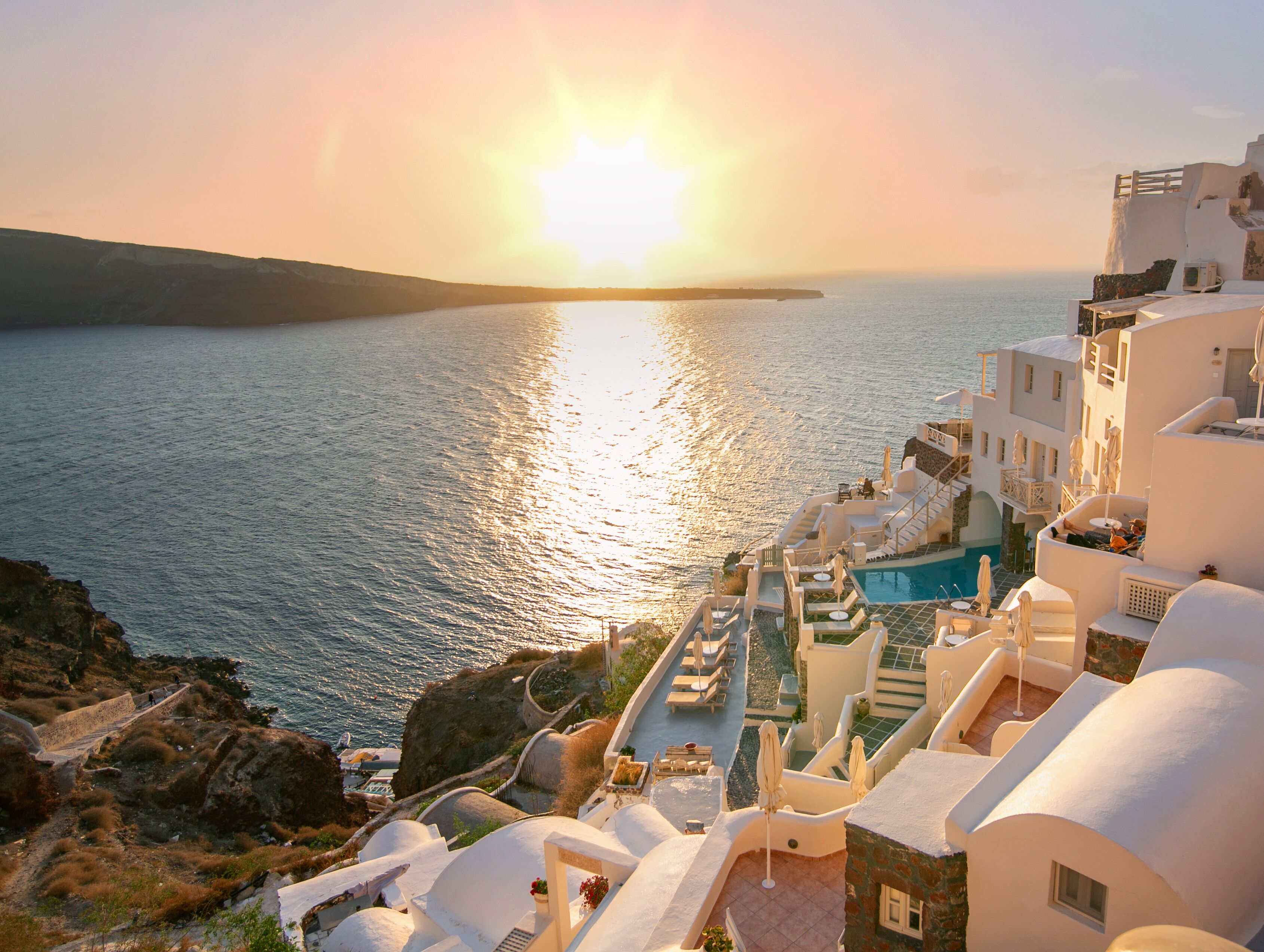 Un hôtel en bord de mer doté d’une piscine, de chaises longues et offrant une vue sur la mer au coucher du soleil.