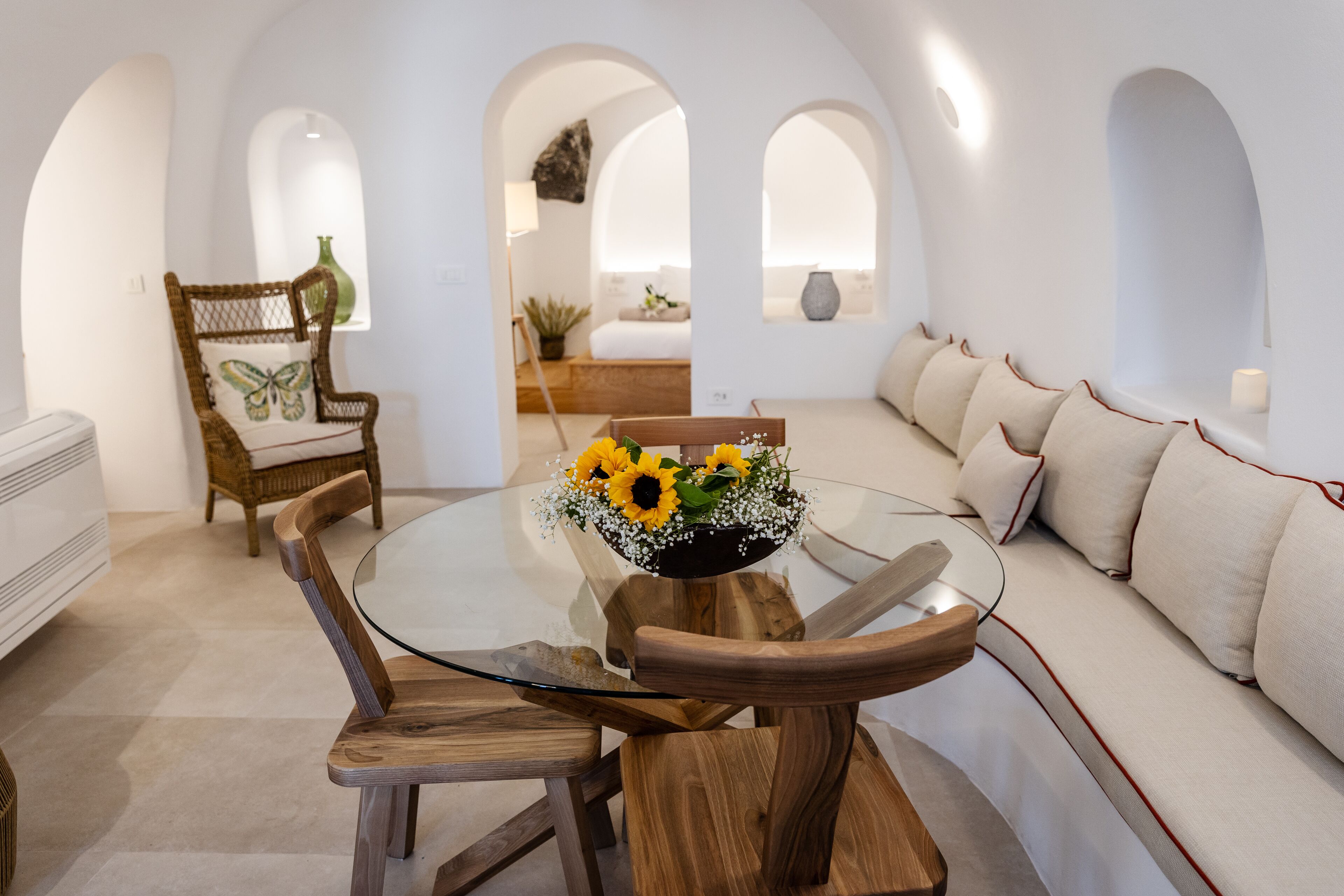 Un coin repas avec une table en verre entourée de chaises en bois, un canapé avec des coussins et un vase décoratif rempli de fleurs.