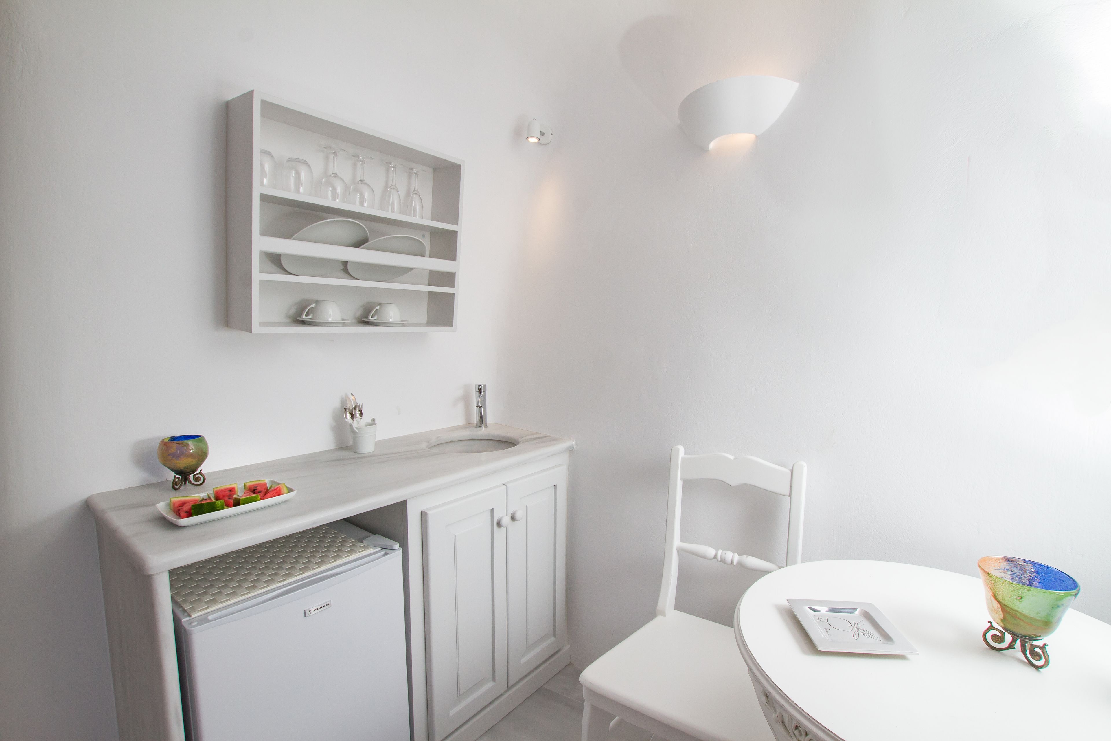 Een witte badkamer met een wastafel, spiegel en planken boven het aanrecht.