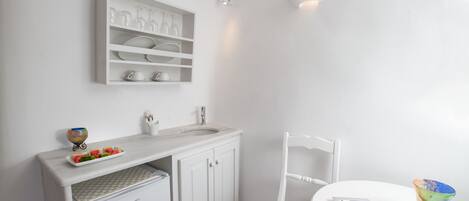 Een witte badkamer met een wastafel, spiegel en planken boven het aanrecht.