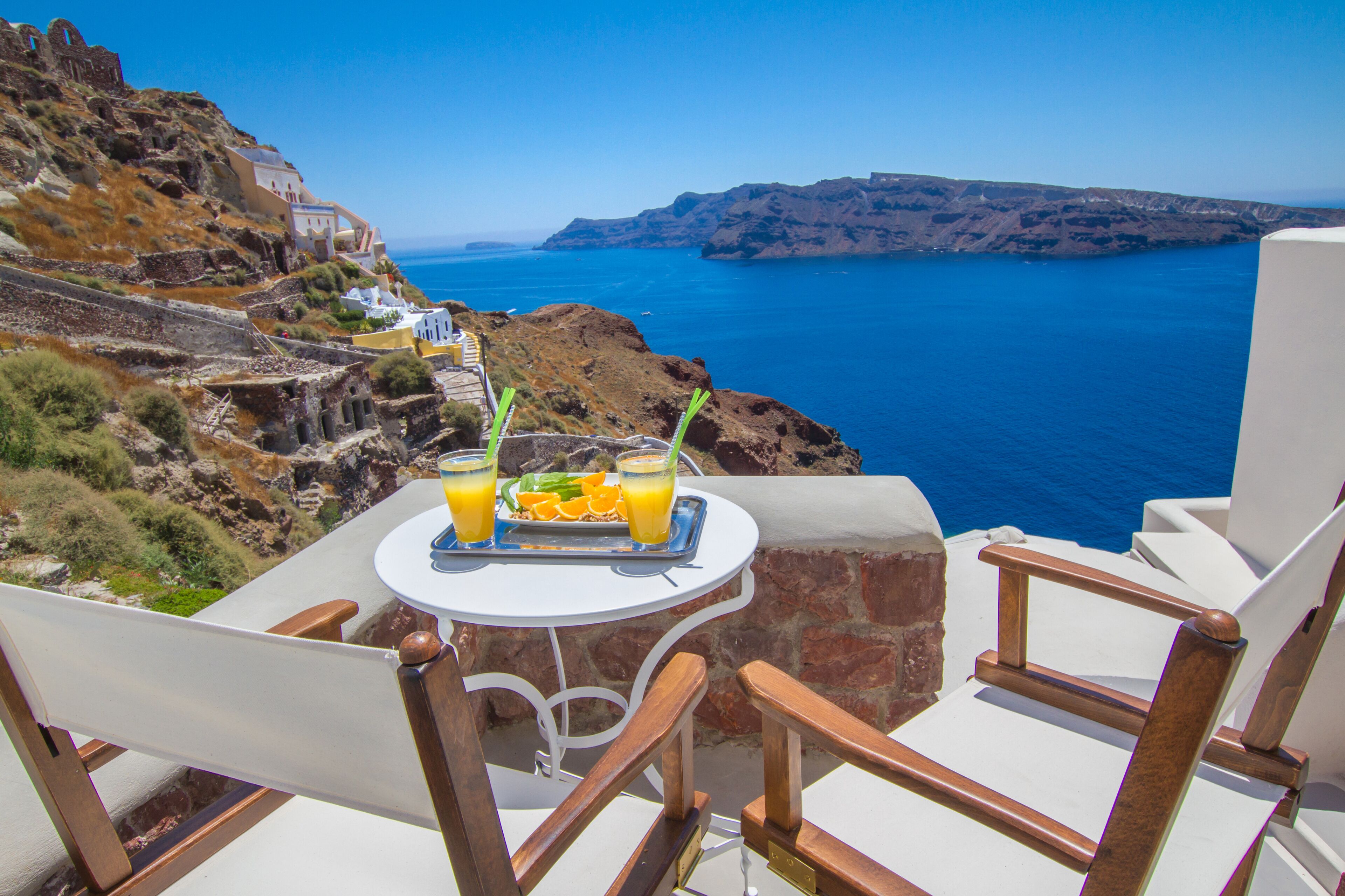 Una mesa con dos bebidas y un plato de comida, con vistas a un paisaje costero con acantilados y el mar.