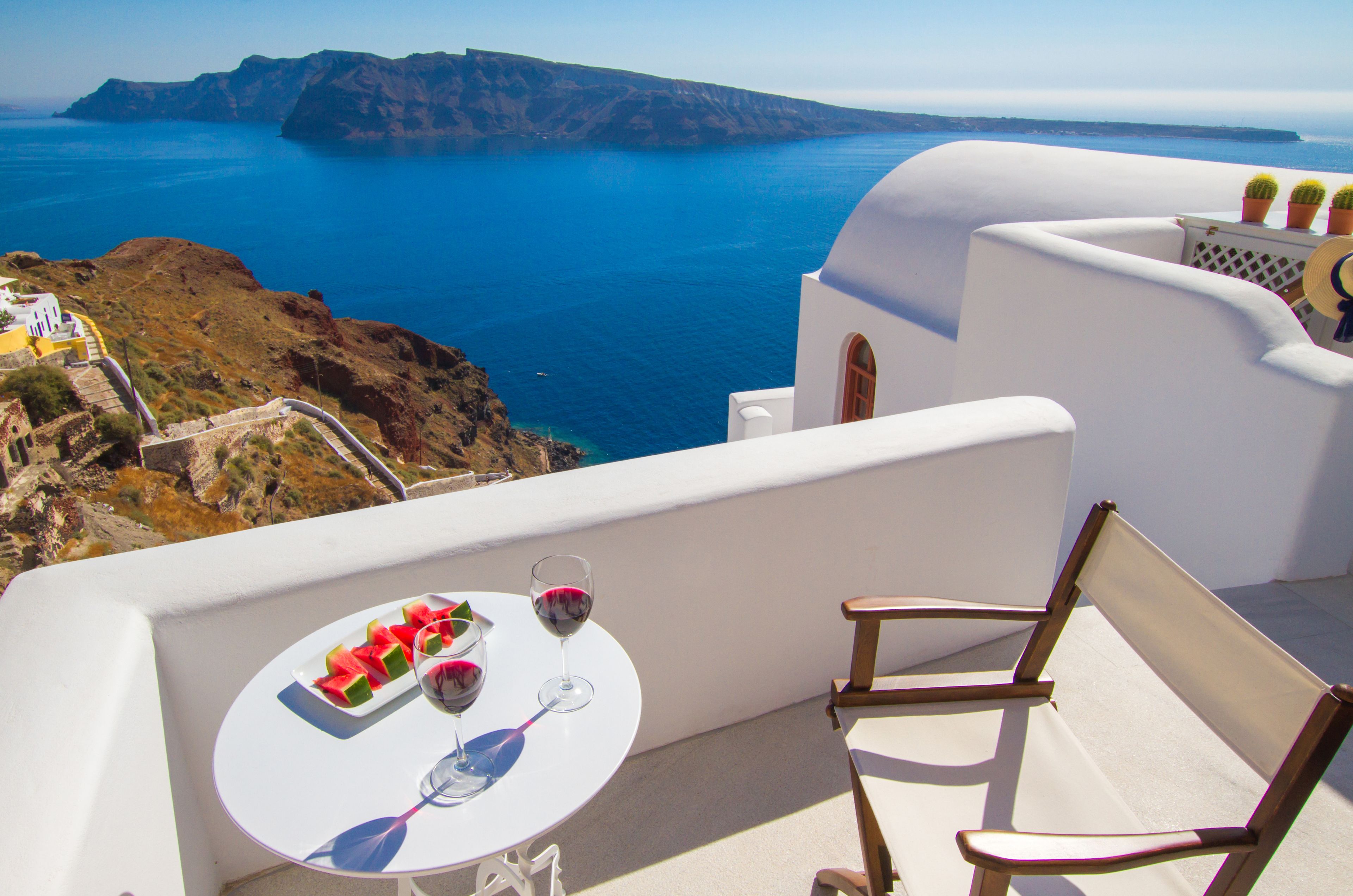 A balcony with a table set for two, featuring a plate of watermelon and two wine glasses.