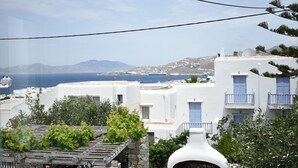 Un village côtier aux bâtiments blancs et aux portes bleues, qui offre une vue sur la mer et sur un navire de croisière.