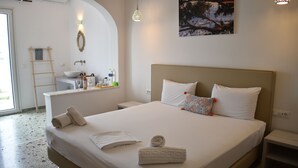 Un lit bien fait, avec des oreillers et des serviettes, une table de chevet, une commode, une salle de bain avec un lavabo et un miroir, et un tableau accroché au mur.