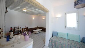 Une pièce comprenant un lit, un coin repas avec des chaises et une table, un petit meuble blanc et une fenêtre avec des rideaux.