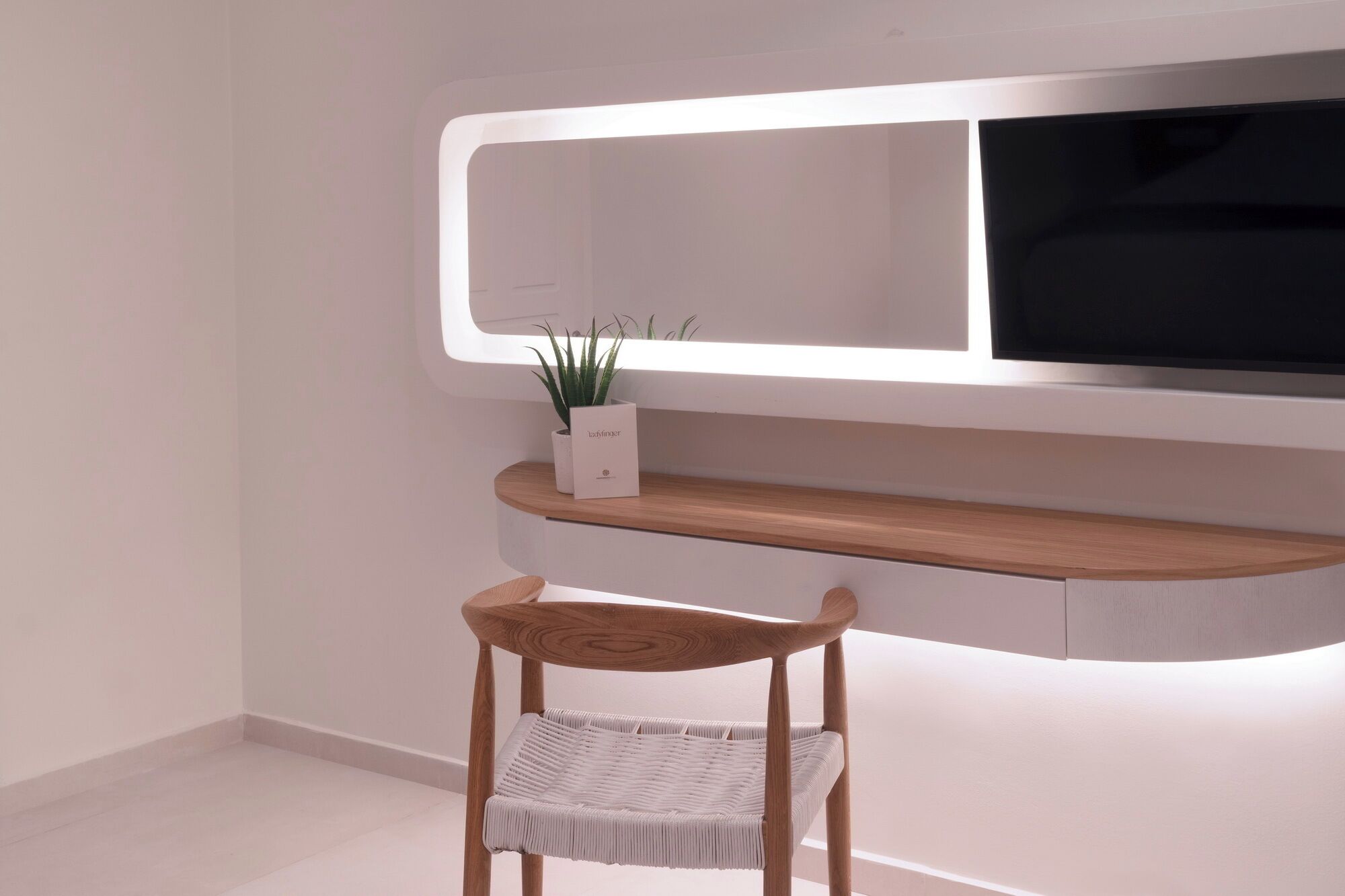 Ein modernes, minimalistisches Zimmer mit einem Holzstuhl, einer weißen Ablagefläche mit einer Pflanze und einem flachbildfernseher, der an einer weißen Wand angebracht ist.