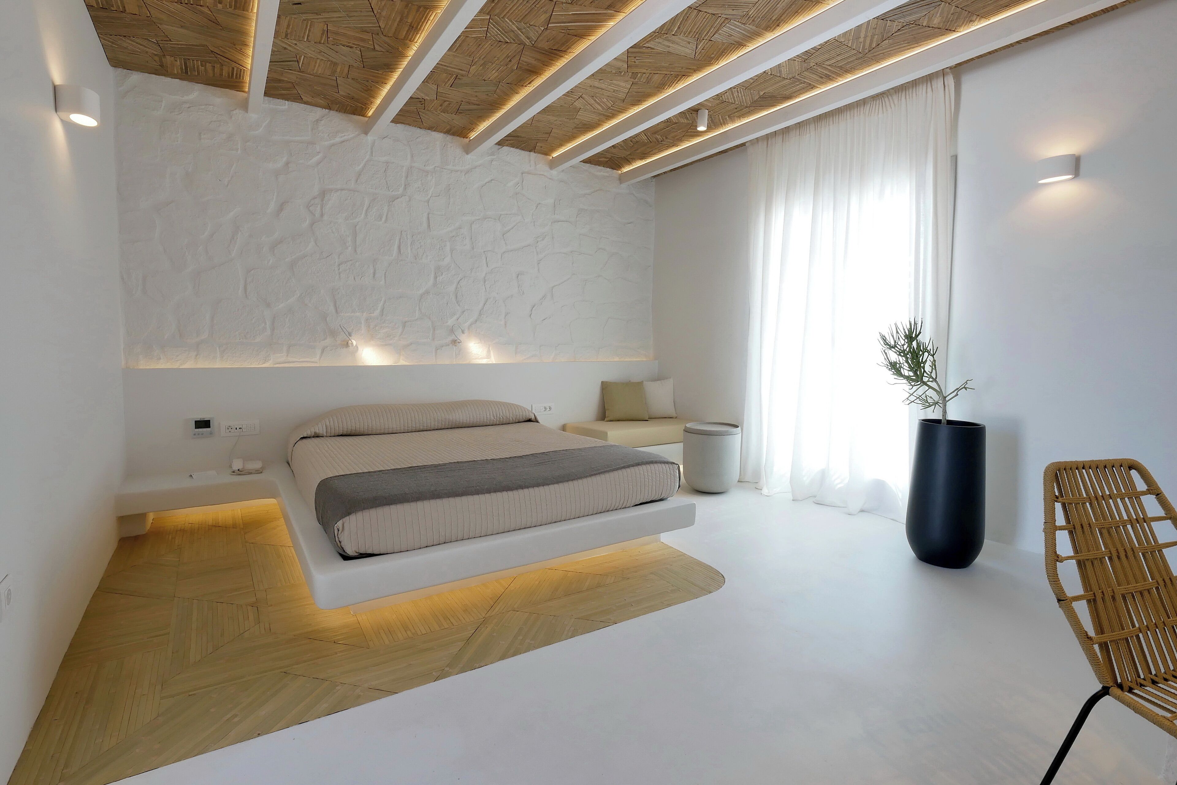 Un dormitorio moderno con una cama empotrada, una mesita de noche, una planta grande en maceta y un aplique de pared.