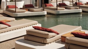 A poolside area with multiple lounge chairs and sunbeds, a clear pool, and a building with balconies and windows. - Andronikos Hotel - Adults Only (Mykonos)