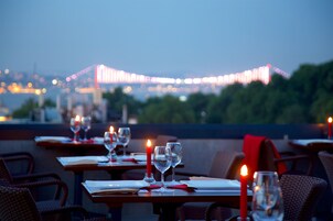 Terraza de restaurante con mesas dispuestas para comer, velas y vista a un paisaje urbano al anochecer.